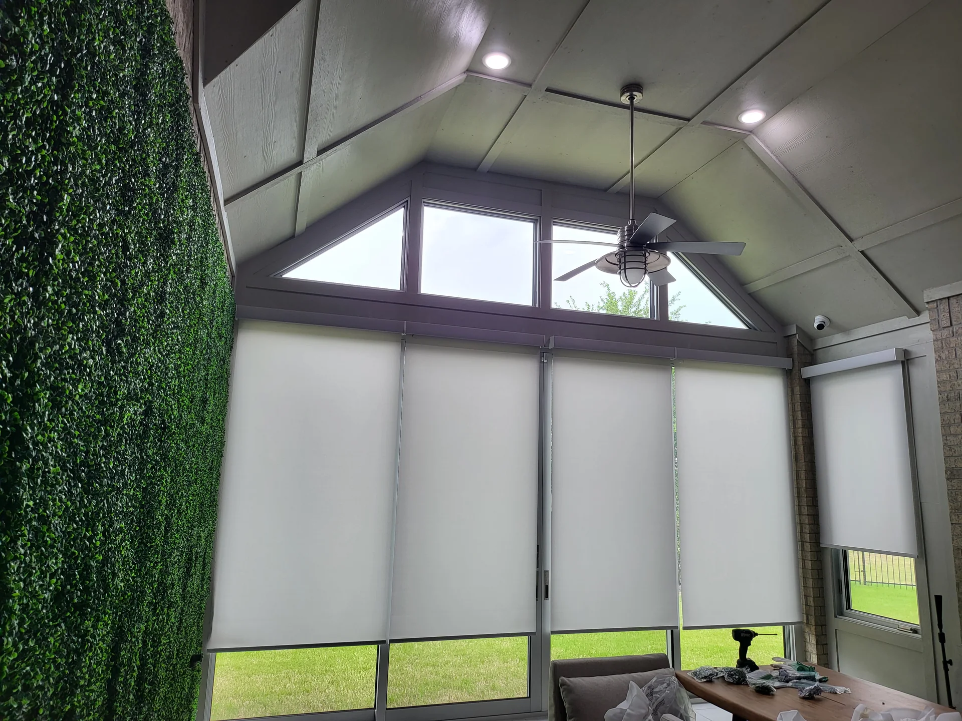 solar shades lowered across floor-to-ceiling windows in a Houston sunroom, softening the light from the yard outside